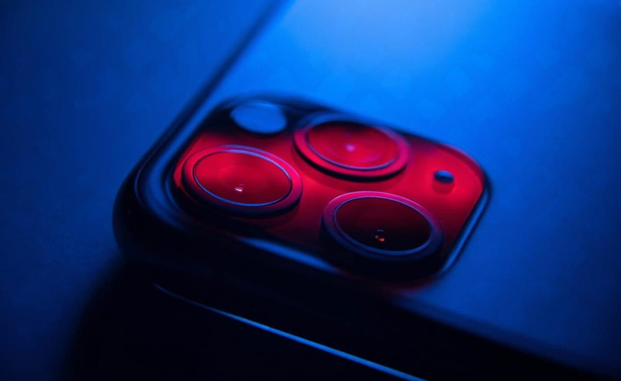 A close-up shot of a modern smartphone camera lens, with a futuristic blue light reflecting off of it.
